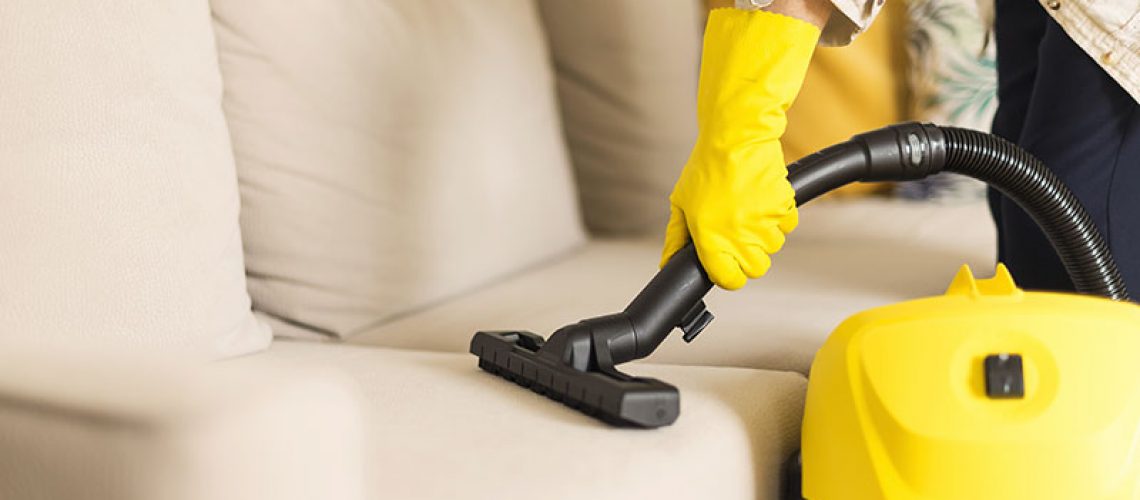 woman-cleaning-sofa-with-yellow-vacuum-cleaner-cop-WKL4JYE-min